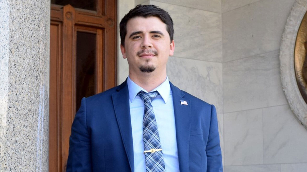 Shawn Gokey dressed in a blue suit wearing a tie and an american flag pin.