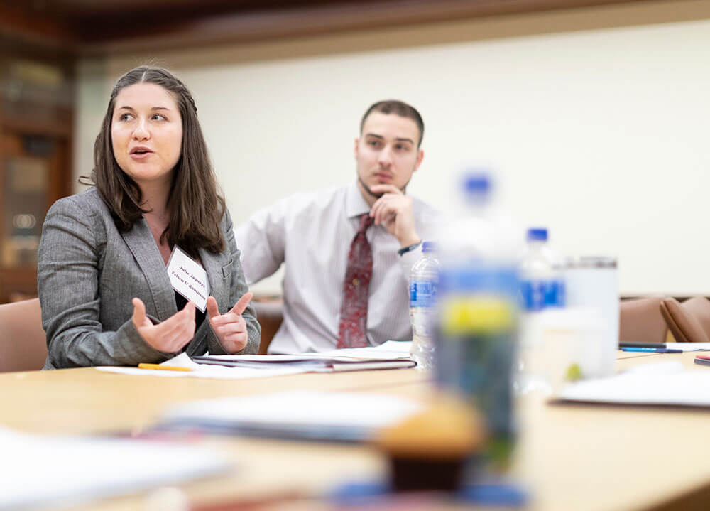 A law student sits at a table during a workshop and interacts with her classmates