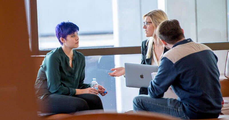 Three law students sit in comfy chairs talking in the Quinnipiac School of Law Center